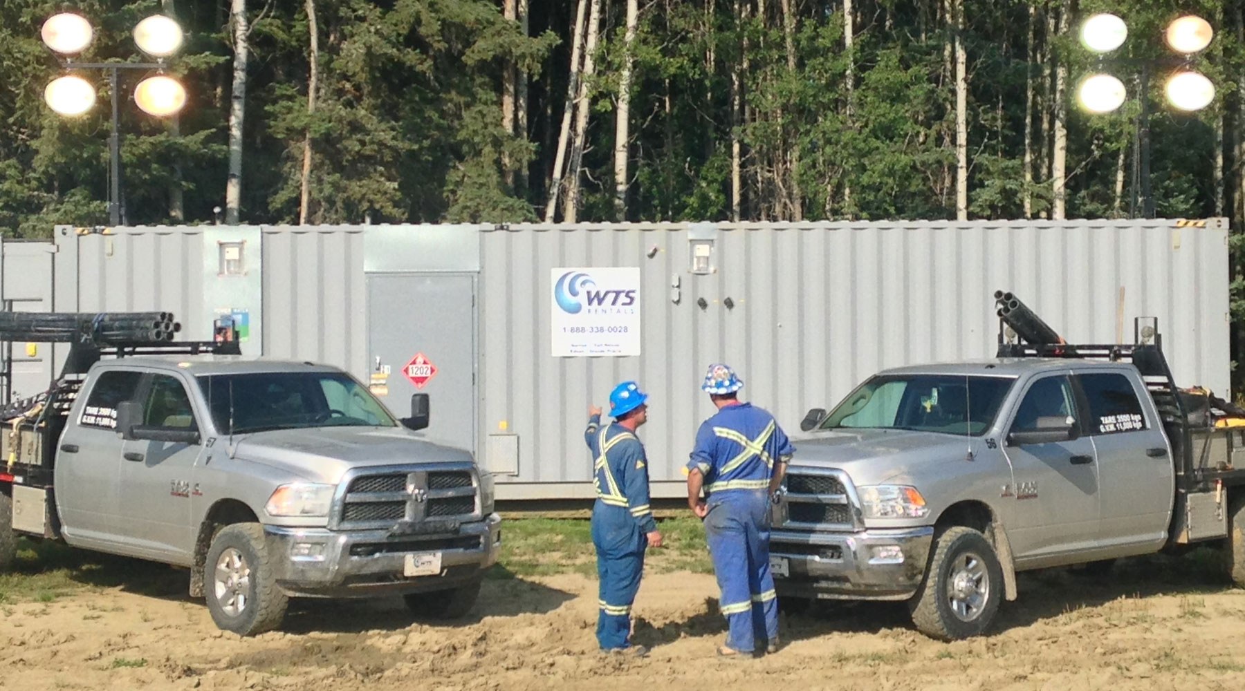 Two workers in blue PPE standing in front of a WTS-branded work trailer Two workers in blue PPE standing in front of a WTS-branded work trailer