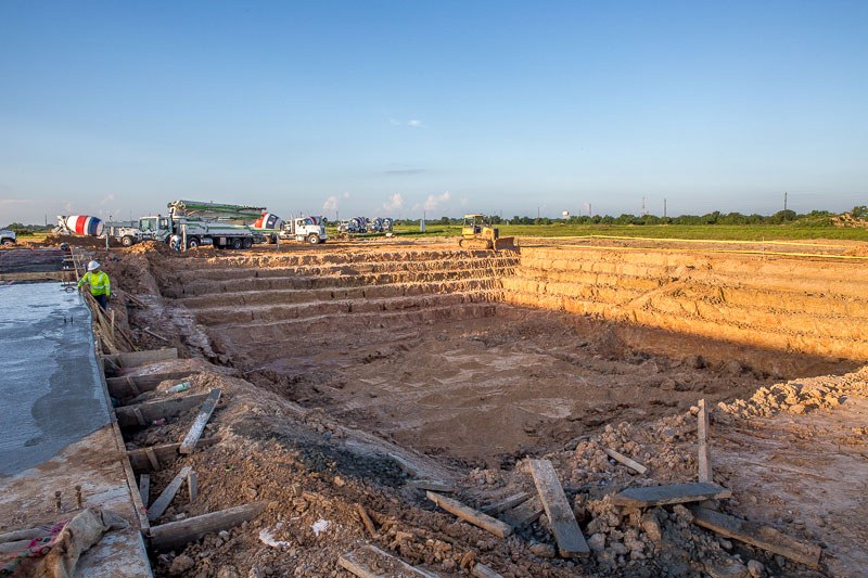 Image of a large outdoor construction area with person wearing a white hardhat and green jacket in background