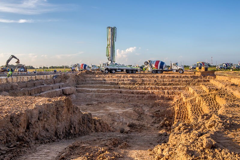 Image of large outdoor construction area with excavator, cement truck, and more equipment in the bakground